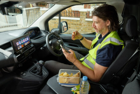 A van driver eats lunch inside his peugeot partner while looking at his phone as peugeot research shows 55 of van drivers typically spend their lunch break scrolling social media